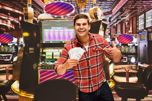 Waist up of with brown hair caucasian young male standing wearing rolled-up sleeves who is excited and celebrating who is pointing and holding us currency