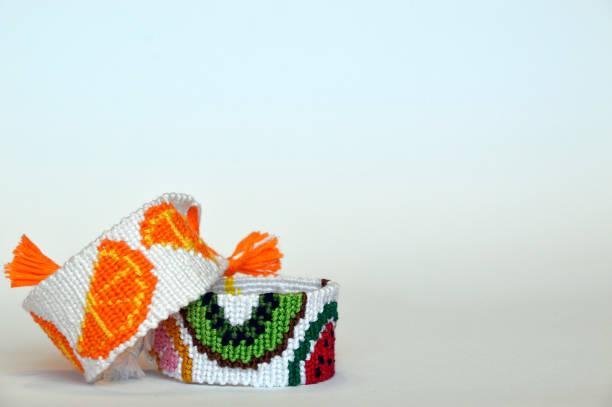 Handmade friendship bracelet with fruit pattern under bracelet with orange fruit pattern on gradient (blue,white,gray) background. Copy space