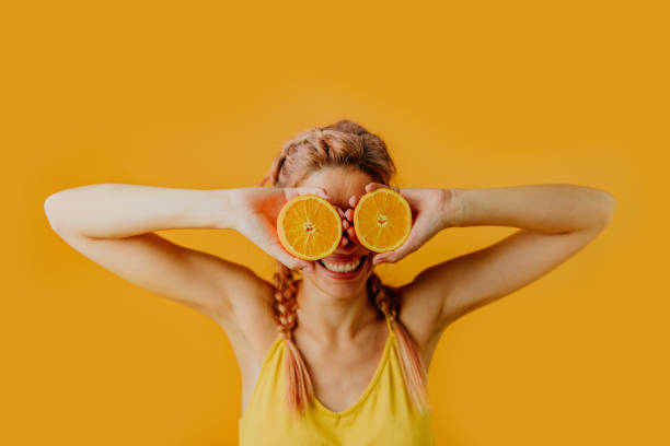 Oranges in her eyes Photo of a playful young woman holding orange halves in front of her eyes; studio shot, isolated on an orange background. photo studio model stock pictures, royalty-free photos & images