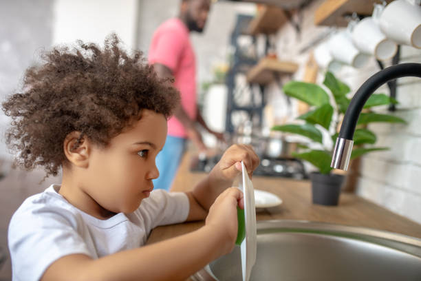istock Pretty curly-haired kid washing the plate and looking concentrated 1227490802