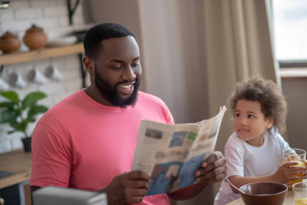 istock Dark-haired african american father reading a newspaper while having breakfast with his daughter 1227490865