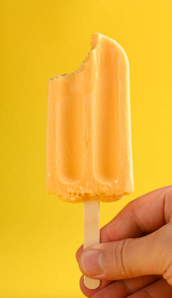 istock hand holding a mango pudding flavor popsicle with a bite on a yellow background 1227492915