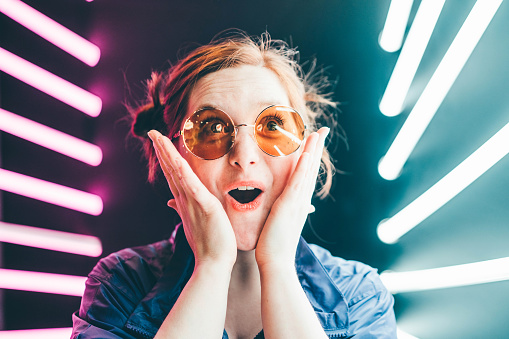 Girl in sunglasses looking surprised on neon background.