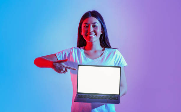 istock Smiling asian girl points finger at laptop with luminous screen 1227499347