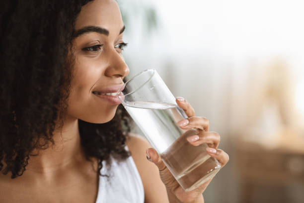 健康な液体。笑顔の黒人女性はガラスから水を飲んで目をそらす - water women glass healthy eating ストックフォトと画像