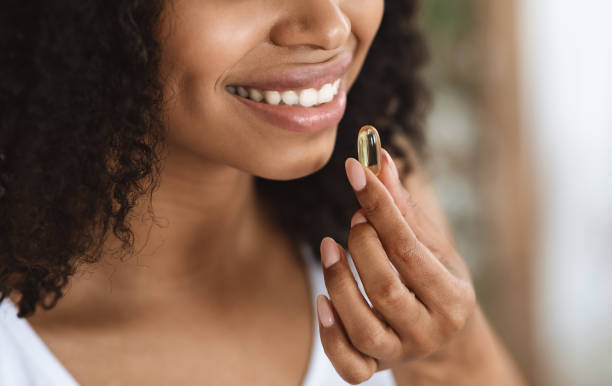 suplemento de belleza. primer plano de la mujer negra sonriente tomando cápsula de píldora de vitaminas - vitamin a nutritional supplement pill capsule fotografías e imágenes de stock