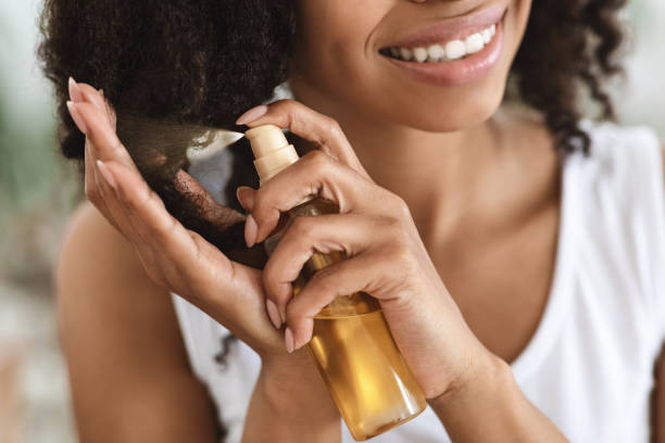 traitement à extrémités fractionnées. femme noire de pulvérisation de sourire d’huile essentielle sur les cheveux bouclés - cheveux hydratation photos et images de collection