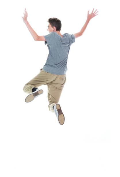 Rear view of aged 12-13 years old caucasian male jumping in front of white background who is feeling joy
