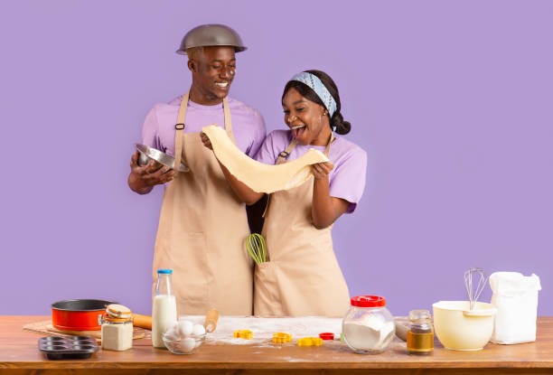 istock Romantic cooking times. Young black couple with dough baking on lilac background 1227502569