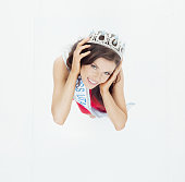Caucasian female beauty queen standing in front of white background wearing sash