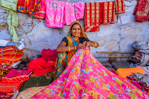 Indian woman selling colorful fabrics on local bazaar, Jodhpur, Rajasthan, India. Jodhpur is known as the Blue City due to the vivid blue-painted houses around the Mehrangarh Fort.