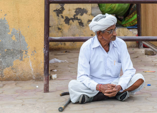 Somnath,  Gujarat, India - December 2018: Portrait of an old man with spectacles, dressed in traditional white clothing, sitting on the floor.