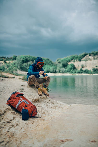 istock Young handsome bearded man sitting near lake and having lunch on camping trip. 1227511607