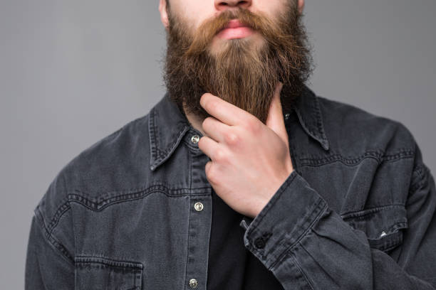 istock Touching his perfect beard. Close-up of young bearded man touching his beard while standing against grey background 1227514546