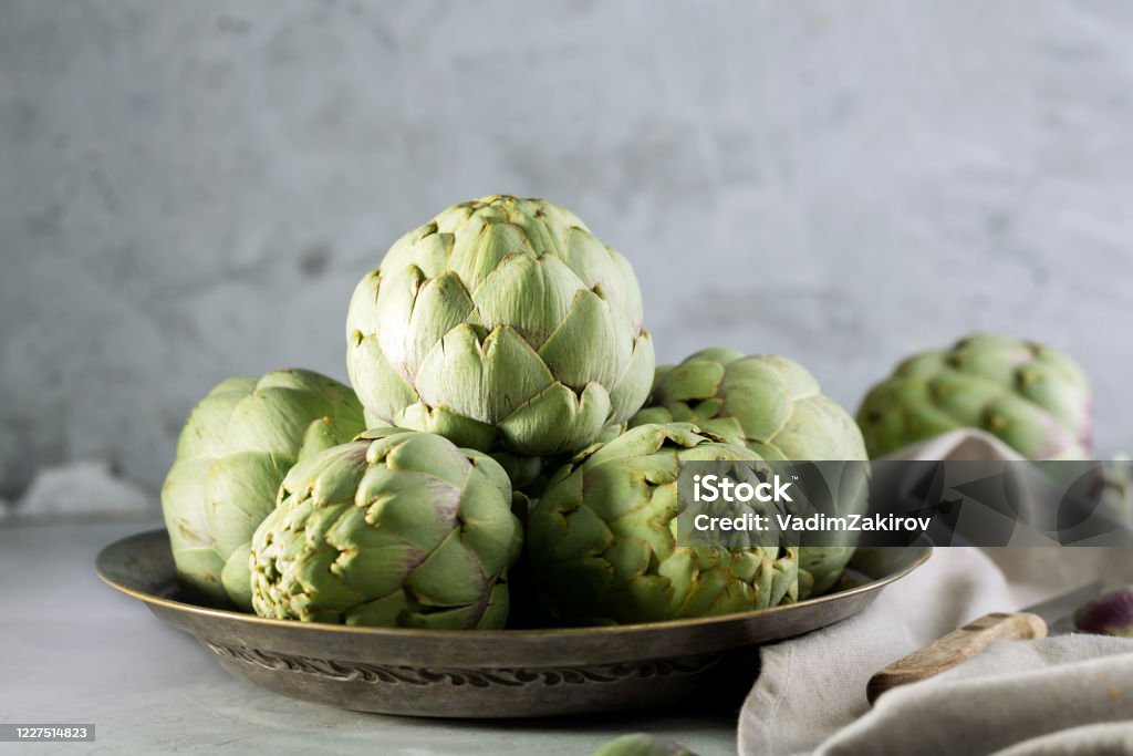 Pile of green Spanish or Italian Artichokes on the metal rustic plate and gray background Pile of green Spanish or Italian Artichokes on the metal rustic plate and gray concrete background, close up Artichoke Stock Photo