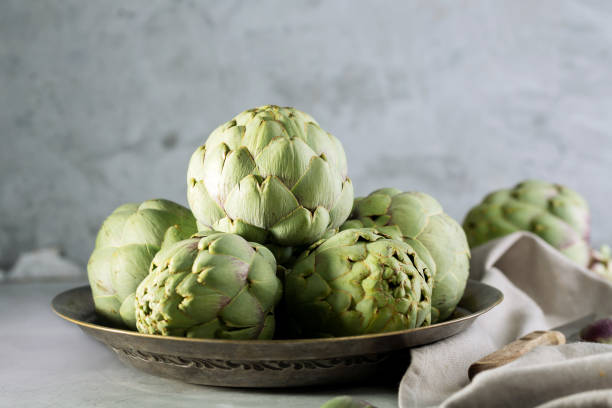 Pile of green Spanish or Italian Artichokes on the metal rustic plate and gray background Pile of green Spanish or Italian Artichokes on the metal rustic plate and gray concrete background, close up Artichoke stock pictures, royalty-free photos & images