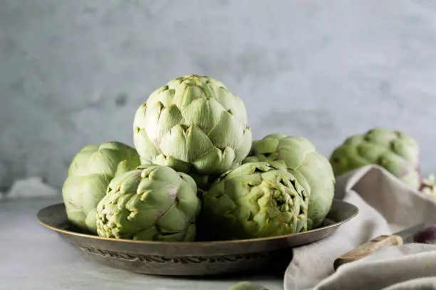 Pile of green Spanish or Italian Artichokes on the metal rustic plate and gray concrete background, close up