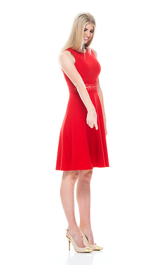 Profile view of aged 20-29 years old who is beautiful with long hair caucasian young women standing in front of white background wearing dress and high heels who is happy who is pointing with hand by side