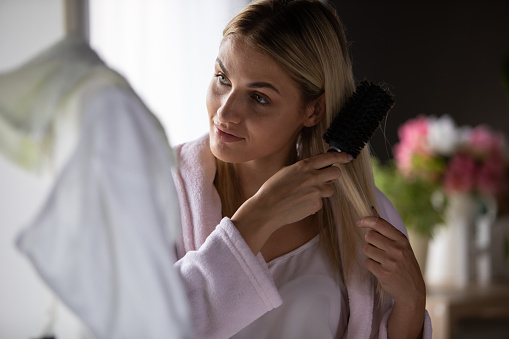 Young woman brushing her hair during her morning beauty routine at home.