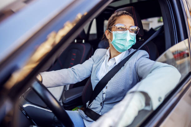 young attractive businesswoman dressed smart casual with protective mask and gloves on sitting in her car and she is ready to drive it. protection from corona virus concept. - illness mask pollution car imagens e fotografias de stock