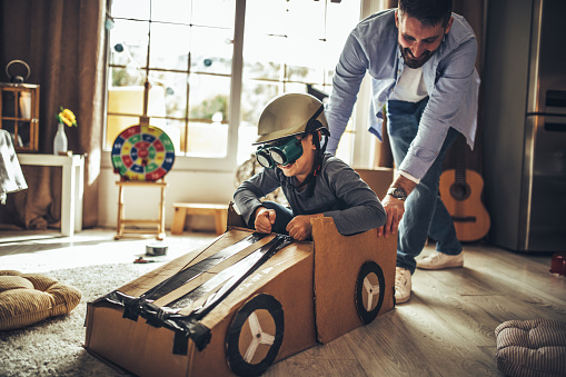 Father and son playing car racing with cardboard boxes