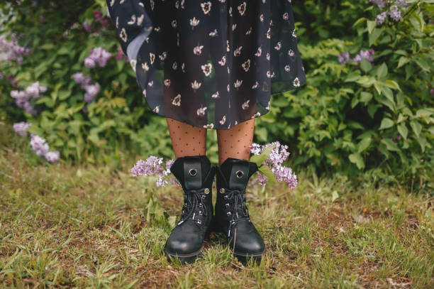 istock Women's feet in black boots stand on the spring grass. Closeup 1227525285