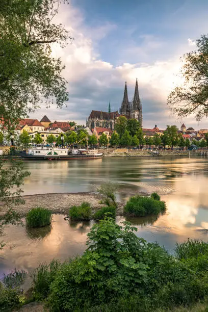 View from Danube river towards Regensburg Cathedral in Regensburg, Germany during late hours of the day with dramatic clouds into the sky and beautiful water reflections. Shot on Canon EOS full frame system.