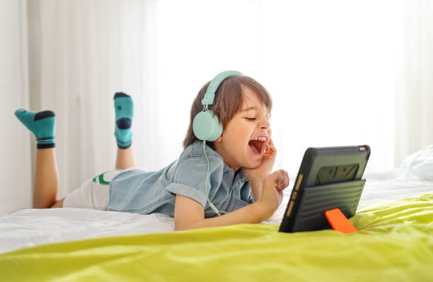 Little smiling boy wearing headphones and using tablet having fun online with his friends in a video call stock photo