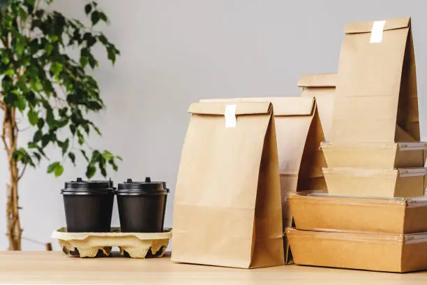 Photo of Many various take-out food containers, pizza box, coffee cups and paper bags on light grey background