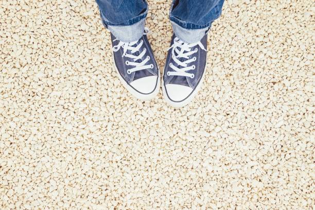 istock Female feet in blue sneakers on a pebble beach 1227533421