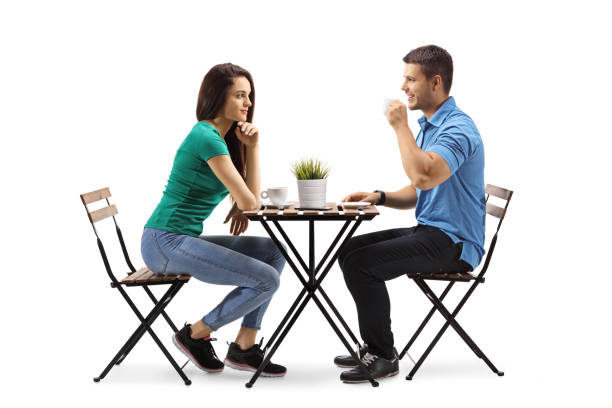 молодой мужчина и женщина сидят за столом и пьют кофе - talking chair two people sitting стоковые фото и изображения