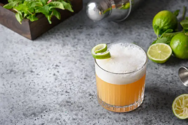 Pisco sour cocktail - whiskey with lime, egg white, sugar syrup in glass on grey table. Space for text.