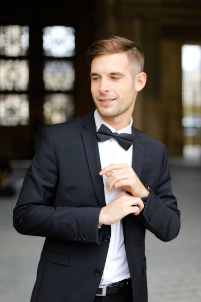 istock Young handsome man standing and posing, wearing black suit and bow tie 1227539805