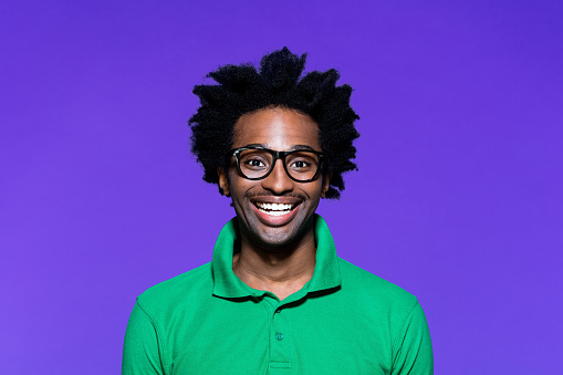 Portrait of surprised afro american young man wearing green polo shirt and nerdy glasses, laughing at camera. Studio shot on violet background.