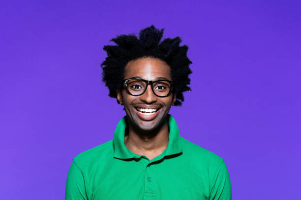 Colored portrait of excited young man with dreadkocks looking away Portrait of surprised afro american young man wearing green polo shirt and nerdy glasses, laughing at camera. Studio shot on violet background. cheesy grin stock pictures, royalty-free photos & images