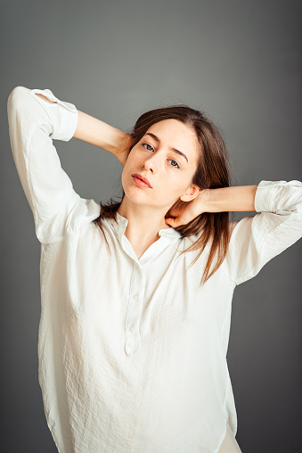 Young girl in a white shirt on a gray background. French woman in white blouse against a background of gray walls. Without retouching.