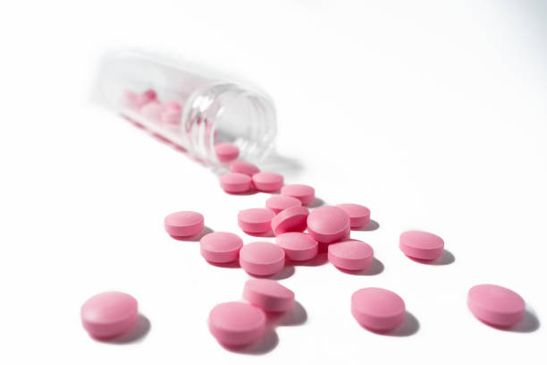 istock Several large bright pink tablets poured from a glass jar on white background 1227548490