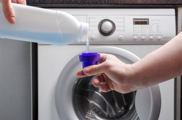 household chores. laundry detergnet puring into the cup against washing machine - liquid soap blue plastic textile imagens e fotografias de stock
