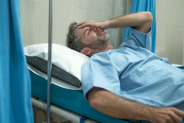 scared and worried man in pain at hospital room - attractive injured man lying on bed suffering painful problem feeling sick and stressed after suffering accident or serious disease stock photo
