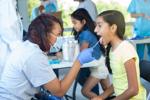 Volunteer doctor checks sick girl's throat During a free clinic at the local park, the mid adult female doctor uses a tongue depressor to check preteen girl's throat.  The doctor wears protective mask and gloves. free of charge photos stock pictures, royalty-free photos & images