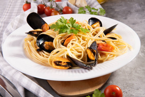 istock Tipical italian pasta spaghetti with mussel and tomatoes on a white plate with ingredients on gray background 1227563015