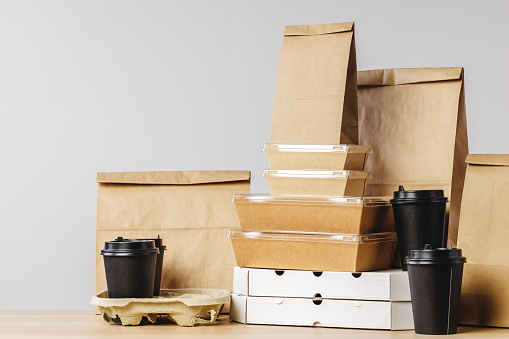 Muchos contenedores de alimentos para llevar, caja de pizza, tazas de café y bolsas de papel sobre fondo gris claro photo