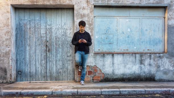 istock Man leaning against the wall looking ay the phone 1227571359