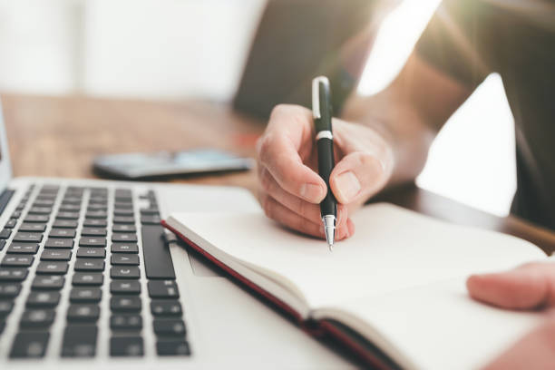 istock person taking notes with pen on paper in front of laptop computer 1227571881