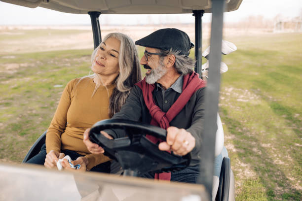 ゴルフカートに乗って、ゴルフをする前に楽しんで幸せなシニアカップル - golf cart golf bag horizontal outdoors ストックフォトと画像