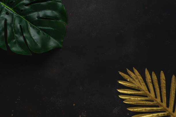istock Creative layout with gold and green tropical palm leaves on black background. Minimal summer abstract pattern. 1227575606