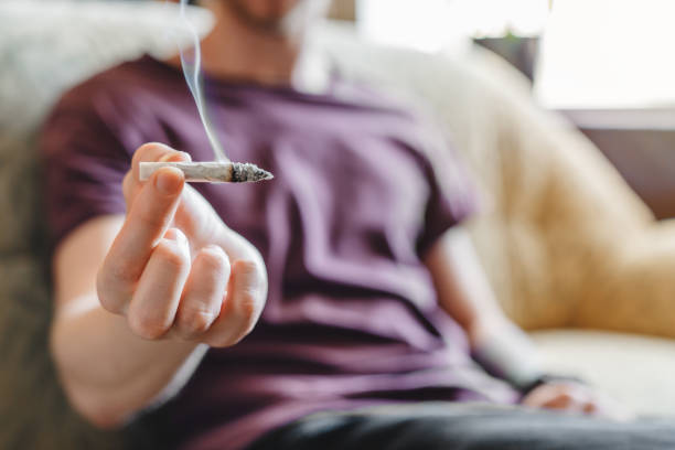 cropped image of young man smoking marijuana or cigarette indoors - tobacco cigarette tobacco product rolling imagens e fotografias de stock