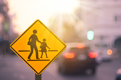 School zone warning sign on blur traffic road with colorful bokeh light abstract background. Copy space of transportation and travel concept. Vintage tone color style.