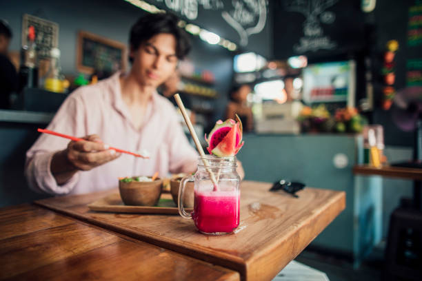 Young Caucasian male sat in an Indonesian restaurant eating chicken skewers with a fruit smoothie.