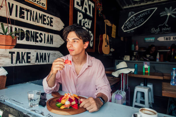 Young Caucasian male sat in an Indonesian restaurant eating chicken skewers with a fruit smoothie.